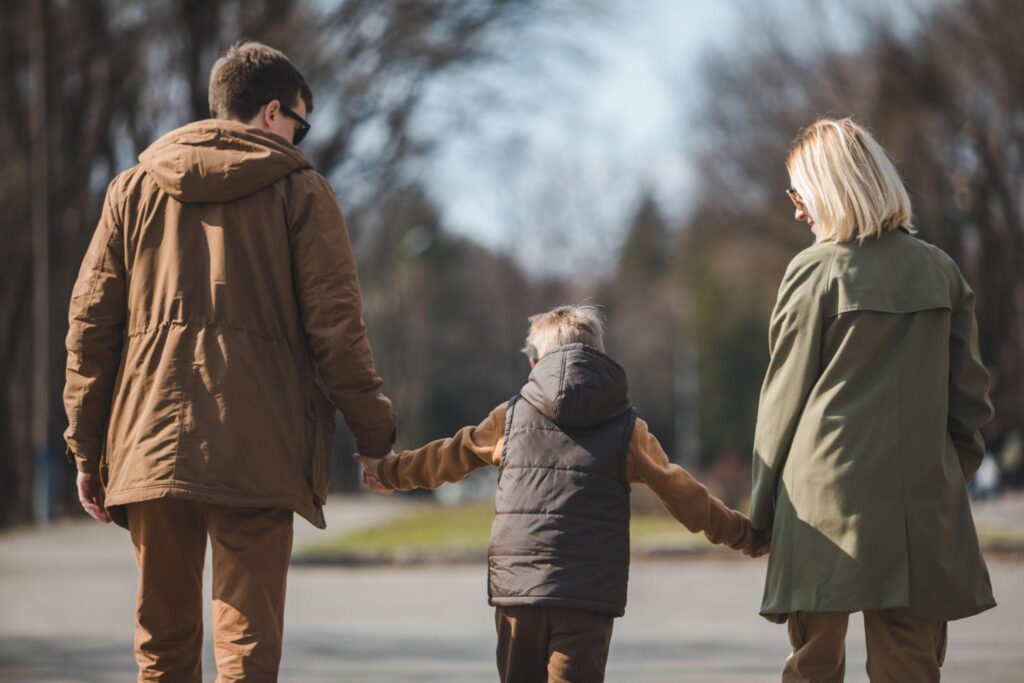 Padre, madre e hijo caminando juntos de la mano, representando la importancia de la cooperación entre progenitores por el bienestar del menor.